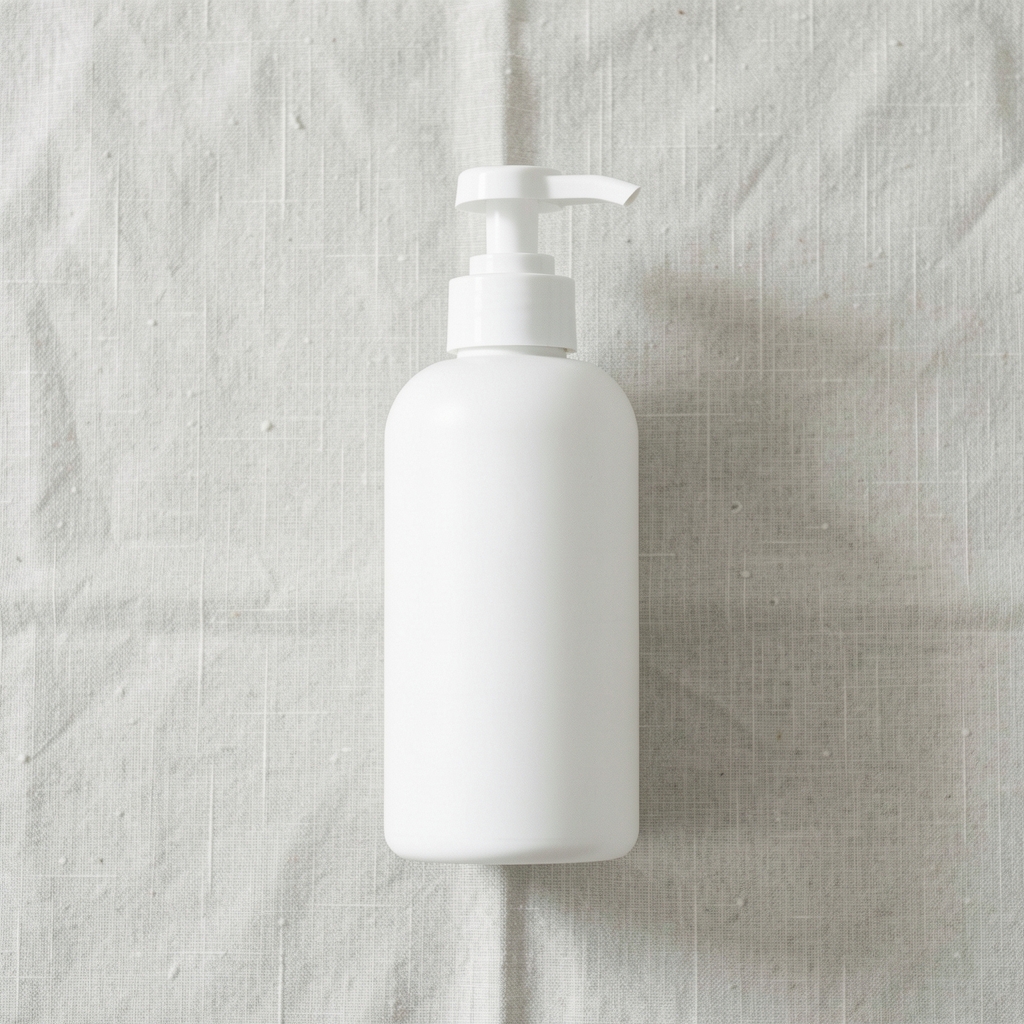 White pump bottle of daily body lotion on a pale linen surface, minimal composition, diffuse natural light